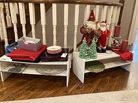 Overall view of two white shelves with Christmas decorations including Santa figures, candles, plates, and napkin rings