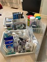 Full view of three plastic baskets containing various cleaning supplies including Clorox wipes, hand sanitizer, Philips brand light bulbs, black casters, and spray bottles.