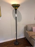 Full view of a tall torchiere floor lamp with green and amber resin shade illuminating the wall above.