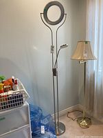 Full view of the tall floor lamp with circular magnifier at the top and smaller adjustable lamp attached to the stem.