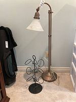Lexington floor lamp with curved bronze metal base and white glass shade beside a black metal bottle rack with six circular holders on a round base