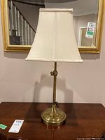 Front view of brass table lamp with beige fabric shade, placed on wooden table indoors.