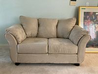 Front view of beige fabric love seat with three back cushions and two arm cushions, showing overall condition and design.