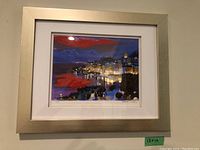 Framed signed print showing a night cityscape with a red sky, illuminated buildings, and reflections on water.