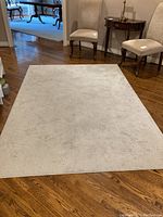 Top-down view of light beige rectangular area rug on wooden floor between two chairs and side table