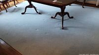 Photo showing blue rug with wooden furniture legs visible, carpet is light blue with some indentations.