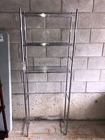 Front view of metal shelving unit with three shelves against concrete block wall showing wear on finish.