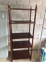 Full view of tall wooden shelving unit showing four shelves and brass finials on corner posts.