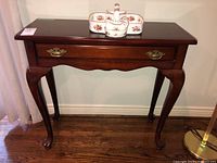 Front view of Bombay Company wooden side table with drawer and claw feet showing polished dark wood finish and brass handles.