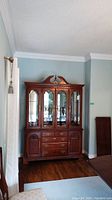 Front view of Stanley wood china cabinet showing four glass doors on top, three drawers and two wood doors below, standing against wall.