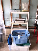Full view of storage shelf with plastic bins, laundry basket, and tray with stand