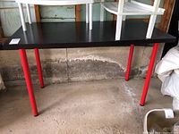 Full view of a rectangular table with a black tabletop and red legs in a garage setting.