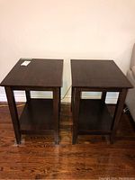Photo showing two dark wood side tables from the front on a wooden floor against a wall.
