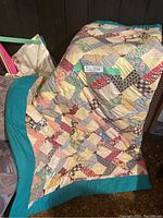 Full view of antique patchwork quilt draped on armchair with teal border and patchwork pattern front visible.