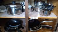 Photo showing a variety of stainless steel pots with lids on upper shelf, and stacked non-stick Teflon frying pans on the lower shelf.