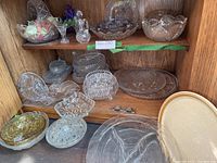 Wide view of multiple crystal and glass bowls, plates and dishes on shelves, showing variety and overall condition