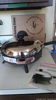 Photo showing the Circulon electric frypan with attached glass lid and box of Pampered Chef round baking stone in background.