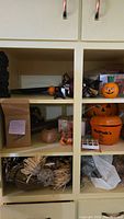 Multiple shelves filled with various Halloween decorations including pumpkin containers, scarecrow figure, smaller pumpkin figurines, and other seasonal decor items.