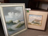 Wide shot of both framed sand dune paintings showing the different frames and ocean scenes with seagulls.