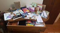 Wide view of wooden table with assorted journals, greeting cards, and pen sets arranged on top and inside an open drawer.