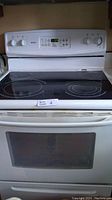White Kenmore electric range front view showing oven door, glass cooktop, and control panel with knobs and digital display.