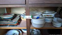 Wide view of shelf holding stacked decorative glass hot plates and assorted Corningware and ceramic casseroles and baking dishes.