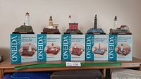 Full set of five lighthouse figurines with their original Oneida branded boxes arranged on a shelf.