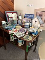 Photo of a table with various lighthouse-themed mugs, small decor items, framed art, and books.