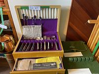 Full view of the wooden case containing the flatware laid out in purple velvet compartments with lids and bonus items visible inside drawer section and around the case.