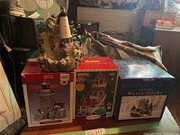 Porcelain lighthouse with water feature and two boxed Lenox Village Collection lighted lighthouse buildings on table