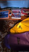 Photo showing selection of canoeing and paddling books along with yellow MEC dry bag and purple dry bag on carpeted floor.