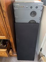 One Wharfedale Mach9 speaker on stand with grille cover on, showing control module and speaker drivers behind grille.