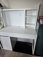 Front view of white IKEA Micke desk with attached top shelf, showing clean modern design and organization features.
