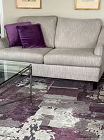 Rug placed under glass coffee table and against a light grey sofa, showing pattern placement and scale in living room.