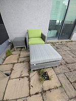 Photo showing the large grey rattan chair with lime green cushions, footstool with striped cushion, and side table on a stone patio.