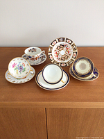 Top view showing all four teacups with saucers and the Imari plate arranged on wood surface