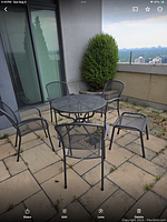 Full set on patio showing round table, four matching chairs with armrests, and two smaller side tables. Set placed on paved outdoor area with a view.
