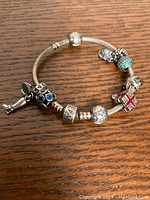 Bracelet with 8 assorted sterling silver Pandora charms arranged on wooden surface.