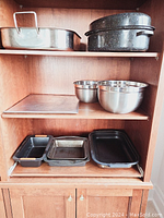 Photo of wooden cabinet shelves holding various baking pans and stainless steel mixing bowls.