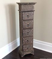 Front angled view of the carved chest showing 5 drawers with geometric and human figure patterns, drawer knobs, and carved detailing on top edge.