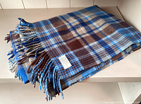 Folded blue and brown plaid wool blend throw blanket with fringe and label visible.