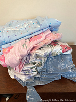 Pile of folded clothing items including light blue pajama with heart print, pink floral pajama, floral satin nightgown, and blue knit robe fabric.