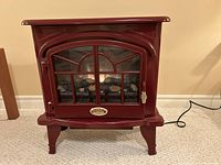 Front view of red electric stove heater with glass door and cord visible to right.