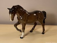 Front and left side view of the brown Beswick horse figurine showing its raised leg and detailed glossy surface.