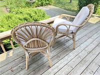 Two wicker rattan armchairs with fan-back design and floral seat and back cushions, positioned on wooden deck