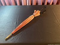 Full length of folded parasol umbrella showing black curved handle and peach fabric.