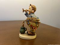 Side view of the child artist figurine holding the painter's palette and brush next to a green pitcher with brushes