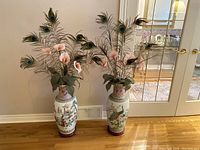 Both vases side by side with peacock feather and floral arrangements, full room context