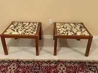 Pair of teak side tables with marble tops side by side on carpet against wall