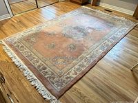 Full view of the vintage pink background Chinese rug with cream floral border laid on hardwood floor.